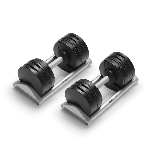 The Bells of Steel NÜOBELL-S Adjustable Dumbbells, featuring black plates and silver handles, rest on a matching silver rack—an ideal addition to any home gym, set against a clean white background.
