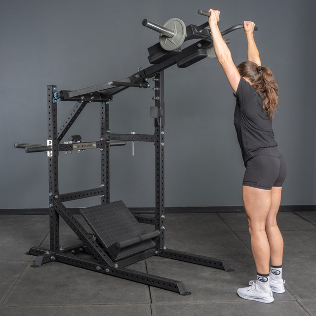 Someone in athletic wear grips the handles of the Bells of Steel Pandemonium Squat – a 3-in-1 Pendulum Squat, Calf Press, and Viking Press Machine. Its sturdy black frame and attached weights make it ideal for any home gym.