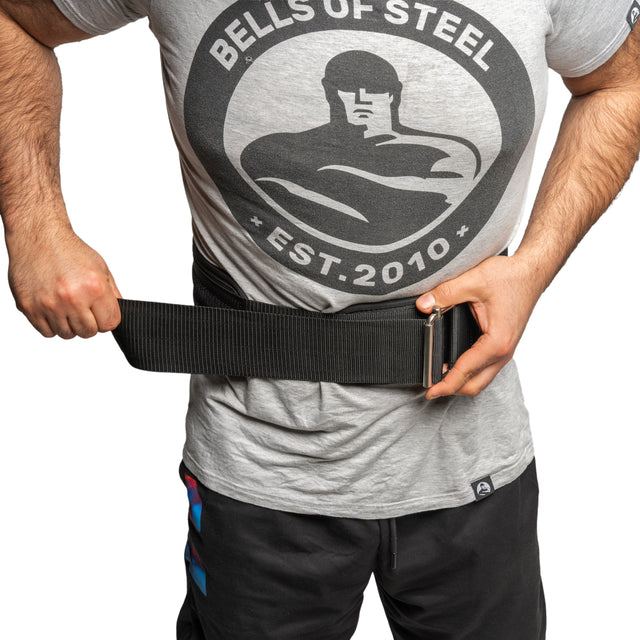 Wearing a Bells of Steel Est. 2010 t-shirt, someone fastens a Bells of Steel Self Locking Belt around their waist, ensuring secure back support for their fitness journey.