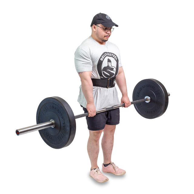 A man wearing a cap, glasses, t-shirt, shorts, and a Bells of Steel Self Locking Belt with a velcro strip holds a loaded barbell in front of him, preparing to lift against a plain white background.