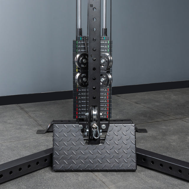 Close-up of the Bells of Steel All-in-One Trainer’s weight stack with numbered plates and metal pulleys, set against a gray wall and tiled floor—ideal for any home gym.