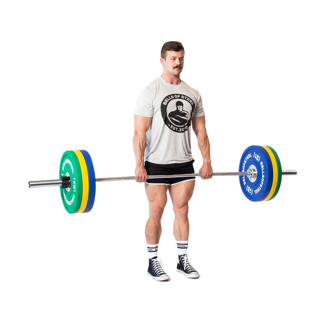 A man in a gray t-shirt, shorts, and sneakers is lifting a barbell loaded with Bells of Steel Urethane Bumper Plates on a white background.