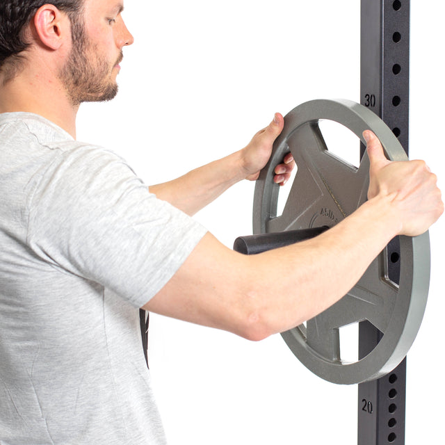 A person in a light gray t-shirt loads a gray, labeled weight plate onto the Bells of Steel Utility Horn Rack Attachment—a squat rack accessory designed for convenient Olympic weight plate storage.