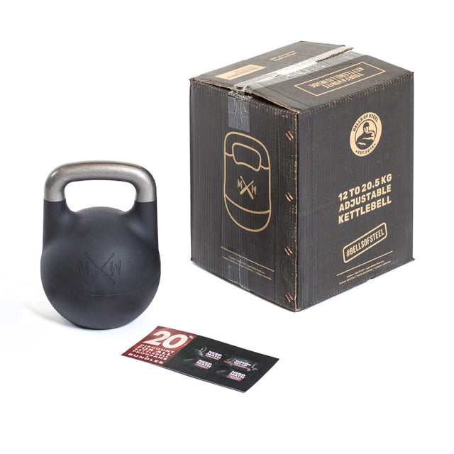 A black Bells of Steel Mark Wildman Adjustable Kettlebell with a metallic handle sits by its box displaying product info, while a pamphlet featuring Mark Wildman’s red and black graphics lies in front of this competition-style kettlebell.