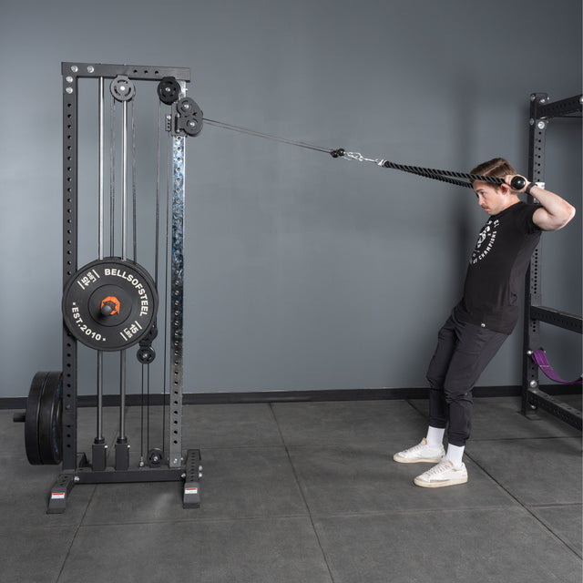 A man in athletic wear uses the Bells of Steel Extra Long Tricep Rope Extension (137cm) to perform a cable face pull at the gym, pulling the attachment toward his face while standing and leaning slightly backward.