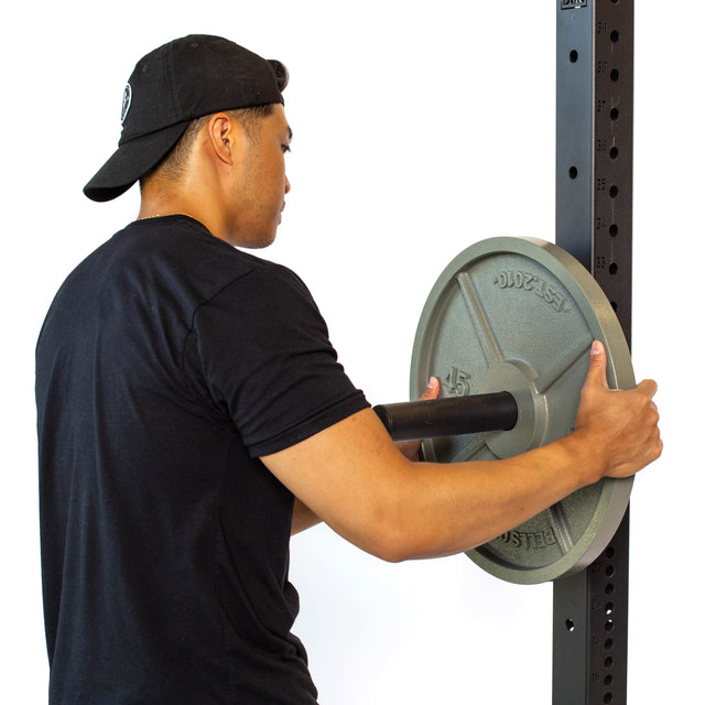 A man in a black T-shirt and cap slots an Olympic weight plate onto the Bells of Steel Utility Horn Rack Attachment, using the vertical storage peg for seamless organization.