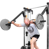 A man in a gray t-shirt and black shorts performs a Jammer Press with weighted bars using Bells of Steel Cable Tower Squat Stands in his home gym against a plain white background.