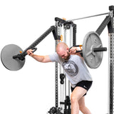 A man in a gray shirt and black shorts exercises with Bells of Steel Cable Tower Squat Stands, leaning forward and extending his arms. The plain white background provides an ideal minimalist setting for a versatile home gym routine.