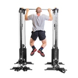 A person in a gray shirt and black shorts performs a pull-up on the Bells of Steel Cable Tower Squat Stands. This versatile equipment, a home gym staple, features dual weight stacks as they use the top-attached bar for lifting.