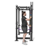 A man in a black shirt and shorts stands inside a black power rack with adjustable safety bars and multiple attachment holes, featuring Bells of Steel Hanging Barbell Holders for efficient barbell storage.