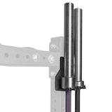 The Bells of Steel Hanging Barbell Holders, in black metal, mount onto a squat rack to securely store two barbells vertically. The faded squat rack and background emphasize the practical barbell storage solution.