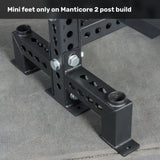 Close-up of the mini feet attachment on a Bells of Steel Manticore Two Post Converter Bench, featuring black metal supports with multiple bolt holes and large bolts securing the bench to a concrete floor.