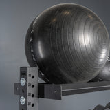 A large black exercise stability ball rests on a Bells of Steel Storage Shelf against a gray backdrop. The ball features circular textured lines with partial white numbers and symbols visible.