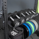 The Bells of Steel Storage Shelves hold several dumbbells, colorful weight plates, a rope attachment, and a 200 lbs sandbag, all displayed against a gray background.