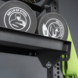 Close-up of two black Bells of Steel weight plates with white logos on a Bells of Steel Storage Shelf, next to a green resistance band hanging from the side.