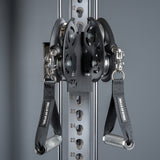 Close-up of a cable pulley attachment with two black "Bells of Steel" handles, mounted on the Oblivyon Tower - 3" x 3” Cable Tower Squat Stands frame with numbered height markers. The background is plain gray.