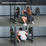 Two people perform barbell squats in the Bells of Steel Manticore Four Post Power Rack - Prebuilt (3" x 3", 1" Holes), using safety bars to catch the weight at the bottom position. Text at top reads, "Safeties act as your spotter.