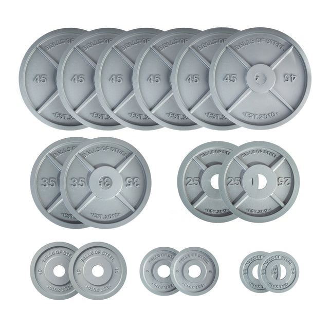 A collection of gray Bells of Steel Machined Iron Olympic Weight Plates, available in various sizes with clearly marked weights in pounds. These slimmer plates are meticulously organized in rows, showcasing the brand and precision hole fit for improved durability and stability.