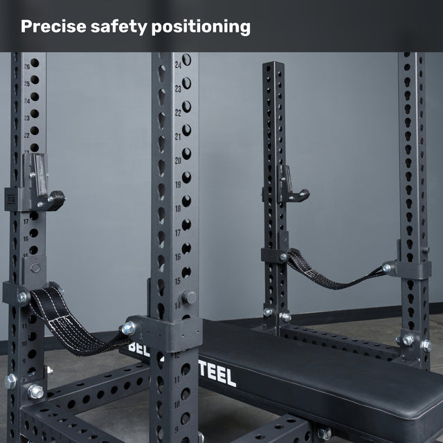 A close-up of the Bells of Steel Manticore Four Post Converter Bench inside a power rack shows adjustable safety straps and multiple numbered holes. The text "Precise safety positioning" appears at the top.