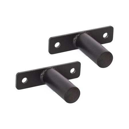 Two black Bolt-On Plate Pegs from Bells of Steel, featuring cylindrical pegs and rectangular bases similar to those used for Olympic-sized weight plates. Each base comes with two holes for wall mounting. The plate pegs are displayed parallel to each other against a plain white background.