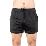 A person wearing Bells of Steel's lightweight and durable black gym shorts is standing against a white background. These shorts, made of high-performance polyester, feature a drawstring, a small logo on the left leg, and text on the right side.