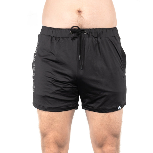 A person wearing Bells of Steel's lightweight and durable black gym shorts is standing against a white background. These shorts, made of high-performance polyester, feature a drawstring, a small logo on the left leg, and text on the right side.