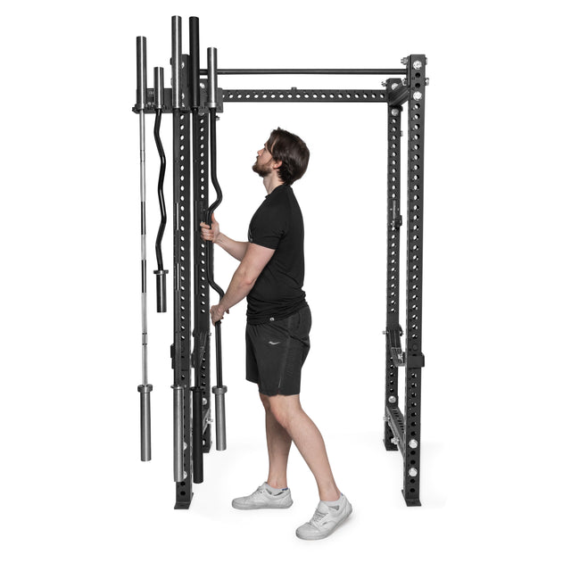 A man in a black t-shirt and shorts organizes several barbells on Bells of Steel Hanging Barbell Holders attached to a power rack.