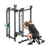 At the gym, a person in a black t-shirt and shorts uses the Bells of Steel Kraken Rack Attachment for 6 Post Hydra Racks. Seated on a bench, they pull cables from the rack's adjustable trolleys with various adjustment options and weights.