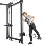 A woman in a gray t-shirt and black leggings performs a leg exercise using the Bells of Steel Kraken Rack Attachment for 6 Post Hydra Racks. She stands on one leg, holding the frame, while extending her other leg back with an adjustable trolley and strap around her ankle.