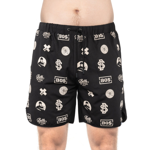 A person is wearing Bells of Steel gym shorts in black with a white "BOS" logo and other symbols. These lightweight, durable shorts feature a drawstring and high-performance, stretchy polyester. The person's torso is partially visible.