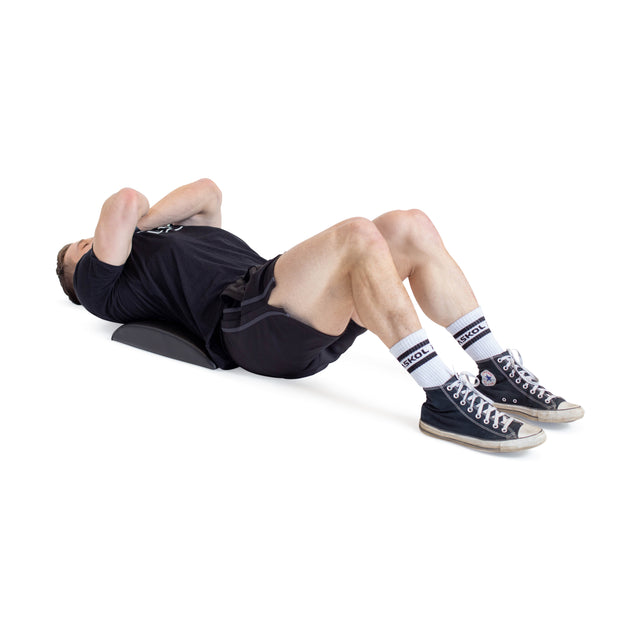 A person wearing a black shirt and shorts, high-top sneakers, and white socks with a blue logo uses the Bells of Steel Sit Up Mat. With knees bent and arms crossed on their chest, they focus on lumbar support for an effective core workout against a crisp white background.