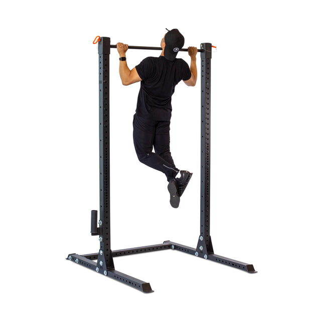 A person in black athletic wear uses the Bells of Steel Adjustable Pull-up Bar Rack Attachment, performing a pull-up on its sturdy base with adjustable settings, supporting their ascent.