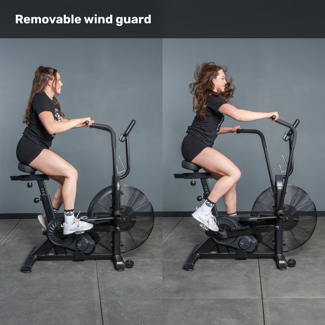 Side-by-side images of a woman using the Bells of Steel Residential Air Bike with Wind Guard in her home gym, demonstrating the removable wind guard, with "Removable wind guard" text at the top.