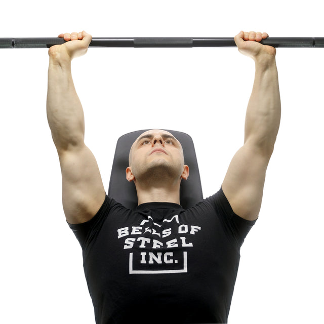 Wearing a black Bells of Steel T-shirt, a person presses the Bells of Steel Alex Leonidas Onyx Bar upward while lying on a bench, viewed from below.