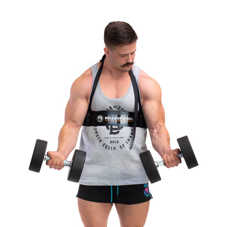 A man with a mustache demonstrates proper bicep curls using dumbbells, clad in a gray tank top and black shorts. He relies on the Bells of Steel Arm Blaster for support, highlighting its aluminum construction against a plain white background.