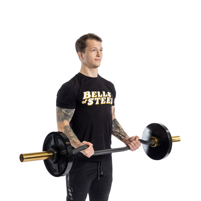 Wearing a "Bells of Steel" shirt, an individual expertly performs bicep curls with the 54.5" EZ Curl Bar. Against a white backdrop, they confidently lift the black barbell with weight plates and gold-colored ends, highlighting impressive arm development.