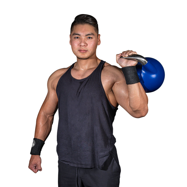 A man in a black tank top and Bells of Steel's BellGuard Kettlebell Wrist Guards confidently holds a blue kettlebell over his shoulder. With wristbands on both wrists, he strikes a pose against a white background, embodying the spirit of dedicated kettlebell lifters.