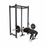 Using Bells of Steel's All-Black Bumper Plates for accurate weight, a person is securely performing a bench press in a power rack while dressed in black clothing and white shoes.