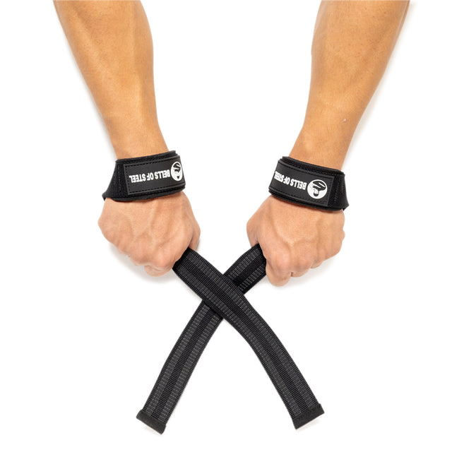 A close-up image depicts two hands equipped with Lifting Straps from Bells of Steel, suitable for weightlifters. The wearer is holding the ends, crossing them in front to boost grip strength. The straps display a logo and the text "BELLS OF STEEL" on a simple white background.