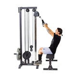 Using the Bells of Steel Cable Tower in their home gym, a person exercises by pulling down the handles for an effective strength workout. They are wearing a black shirt, gray shorts, and black shoes while using the multi-pulley system with a weighted stack.