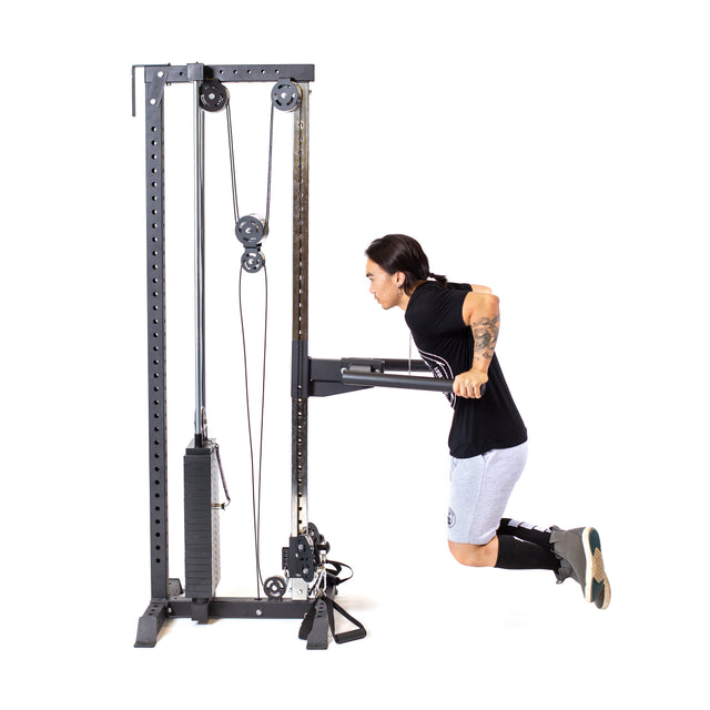 A person in athletic attire, with long hair and tattoos, performs tricep dips using the Bells of Steel Cable Tower. They're wearing a black t-shirt, gray shorts, knee-high socks, and sneakers against a white background, highlighting the effectiveness of cable machine exercises.