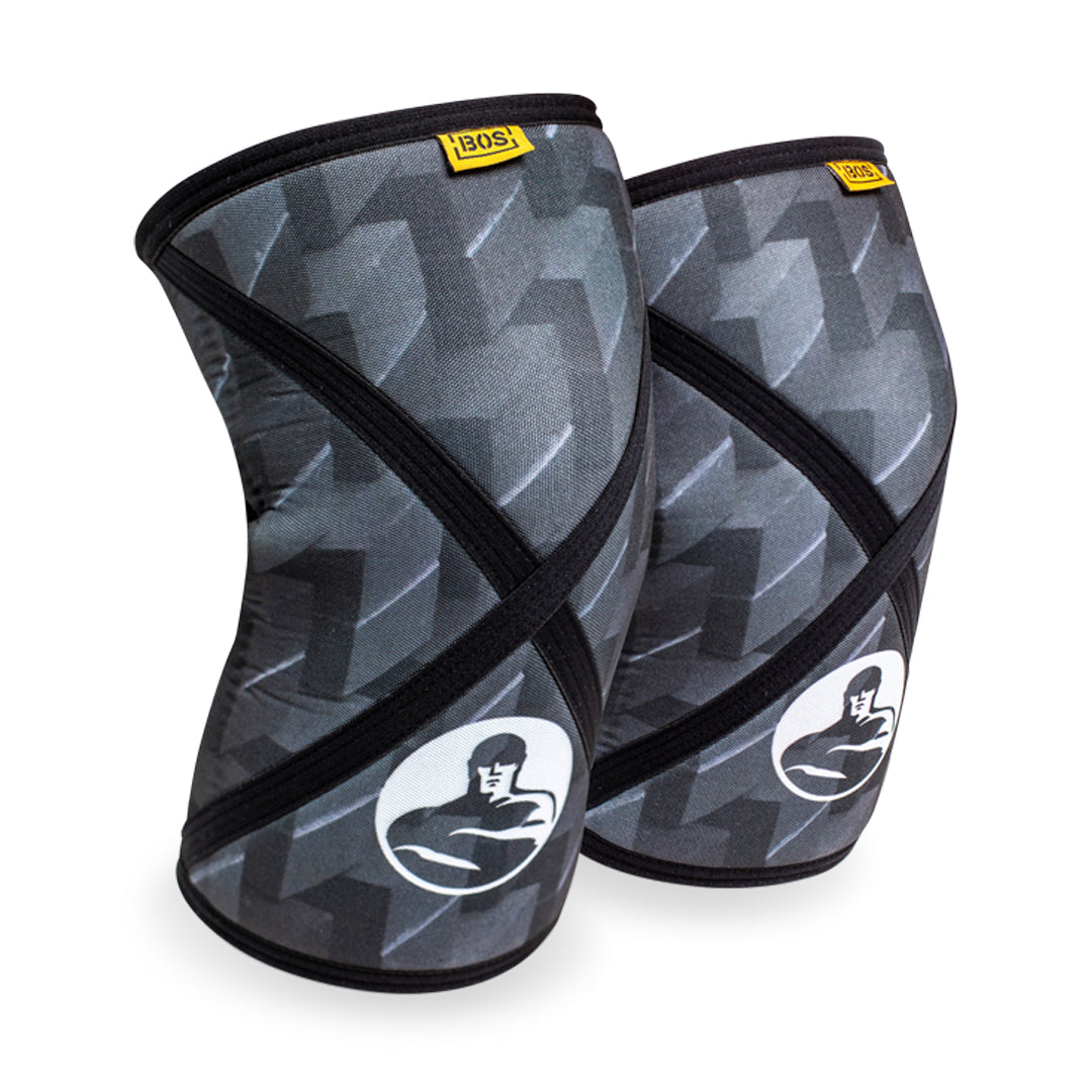 A pair of compression knee sleeves by Bells of Steel, featuring a black and gray geometric pattern with a white logo depicting a muscular figure positioned at the bottom. These sleeves offer excellent support and are stylishly accented with small yellow tags at the top.