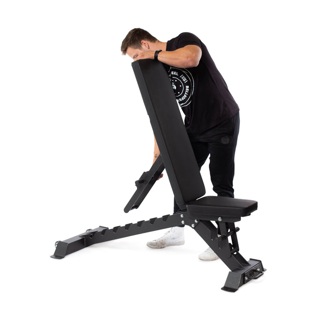 A man in dark pants and a black t-shirt adjusts the Buzz-Saw Heavy-Duty Adjustable Bench by Bells of Steel, setting its backrest to one of 8 angles for an optimal workout.