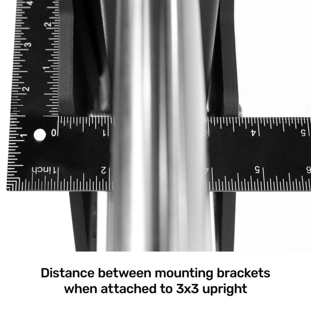 Close-up of two black metal mounting brackets with rulers around a vertical pole, with text, "Distance between mounting brackets when attached to 3x3 upright," ideal for enhancing your Bells of Steel power rack and supporting the Smith Machine Rack Attachment.