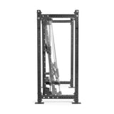 A black-and-silver adjustable workout bench is placed vertically inside a sturdy, multifunctional power rack by Bells of Steel, featuring the Smith Machine Rack Attachment. It includes adjustable pegs and cables for versatile weight training and exercises.