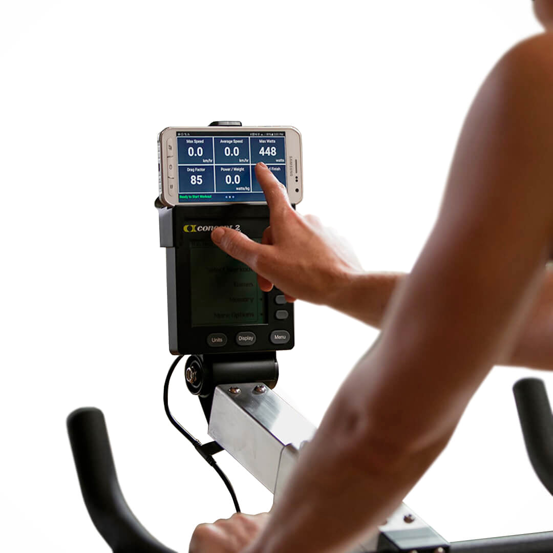 An individual exercises on the Concept 2 BikeERG With PM5 as their smartphone, displaying fitness stats such as distance, speed, and calories burned on the PM5 Performance Monitor, is carefully adjusted for an optimal full-body low-impact workout.