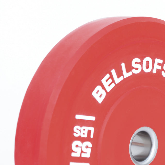 Close-up of a red Bells of Steel Coloured Bumper Plate marked "55 LBS" with a white logo, featuring a stainless steel insert for barbell attachment, set against a white background.