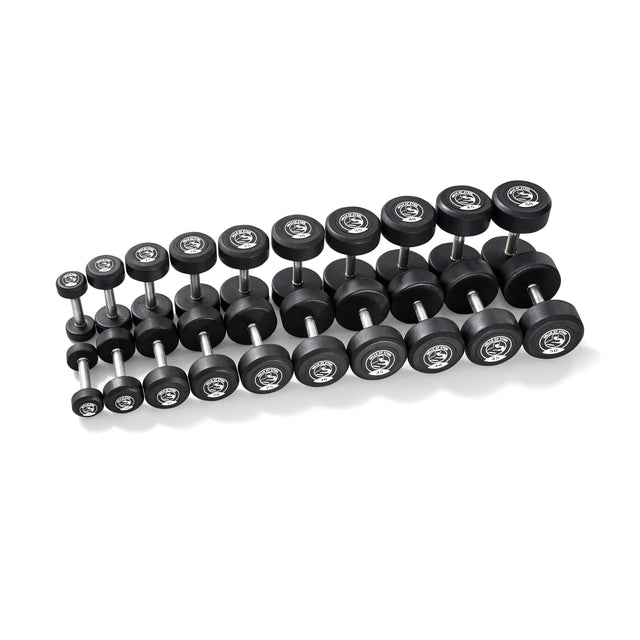 Bells of Steel Urethane Dumbbells, featuring black rubber-coated round heads and metallic handles, are neatly arranged in rows on a white background. The set displays a range of weights from small to large, showcasing their commercial-grade quality and variety.