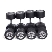 A set of five Bells of Steel Urethane Dumbbells is organized in ascending weights from 85 to 100 pounds. Each dumbbell displays a circular logo with "BELLS OF STEEL" and a flexed arm image on its stainless steel heads.