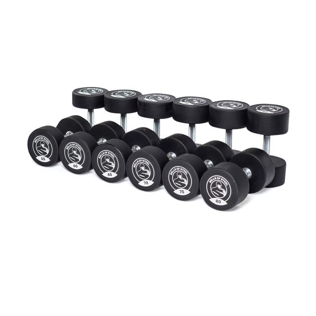 A set of ten Bells of Steel urethane dumbbells, ranging from 45 to 85 in commercial-grade quality, is arranged in two rows on a white background.